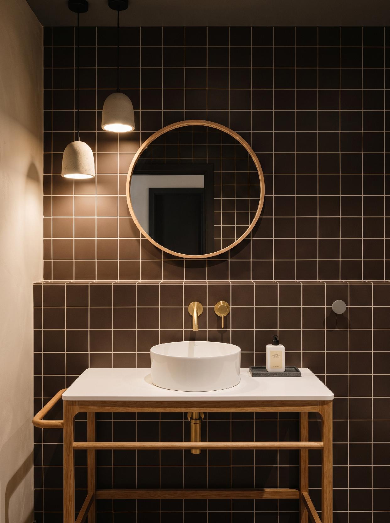 A photograph of a warm, modern, and minimalist bathroom with a graphic tiled wall, captured at eye-level from 