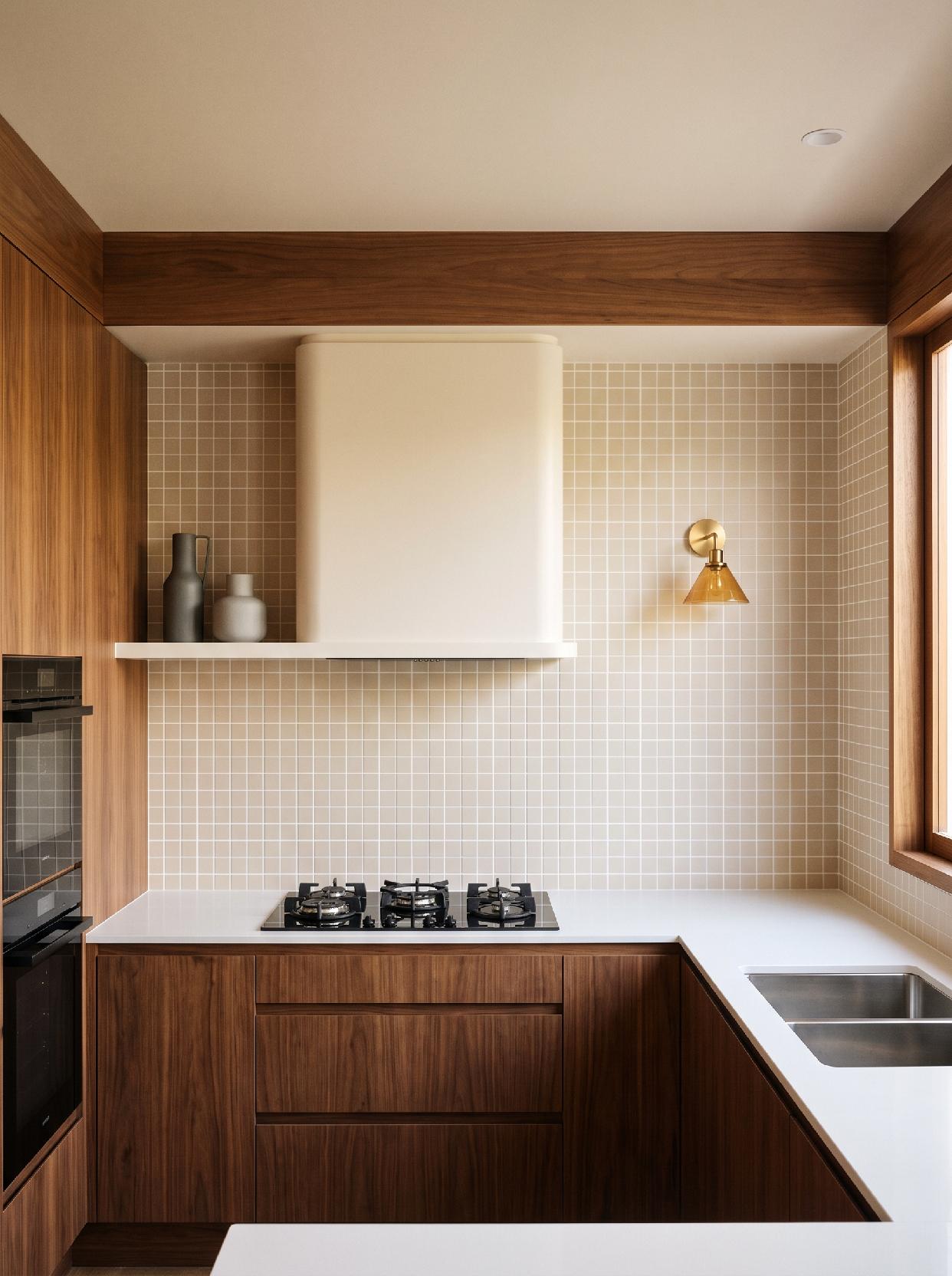 A photograph of a warm and minimalist modern kitchen with natural wood accents and a grid-tiled backsplash, ca